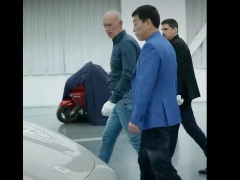 GWM:n hallituksen puheenjohtaja Wei Jianjuan ihmettelemässä lahjaksi saamaansa Xiaomin sähköautoa. Taustalle on 'vahingossa' unohtunut mielenkiintoisen näköinen moottoripyörä. Kuva Wei Jianjuanin Weibo -videolta.